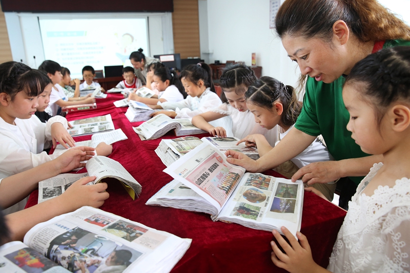 3暑期研学班上，孩子们在志愿者陪伴下学习剪报。（朱华南 摄）