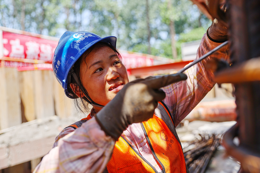 建筑女工将立起来的钢筋绑扎、扭紧。朱其摄