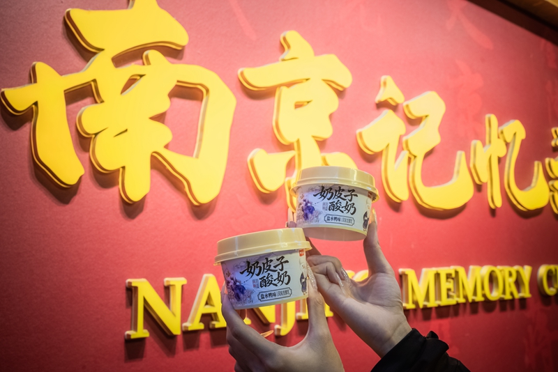 游客手持盐水鸭风味奶皮子酸奶在南京地标拍照打卡。卫岗乳业供图
